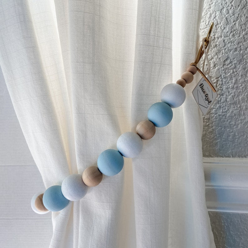 Natural wooden beads curtain tieback in alternating light blue, white, and natural wood colors holding a white curtain.