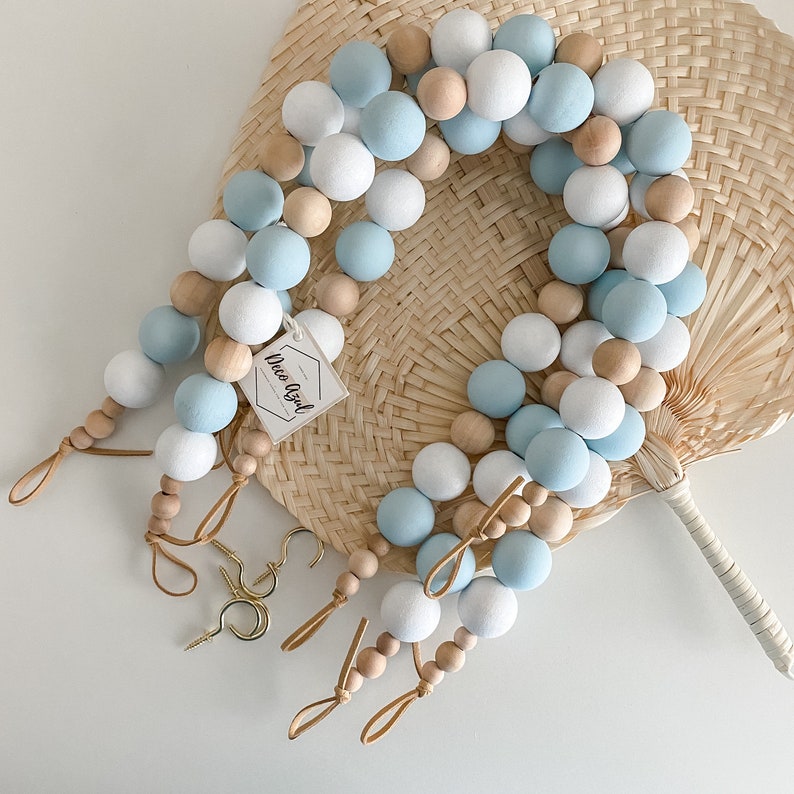 Wooden bead curtain tiebacks with light blue, white, and natural beads, leather loops, and included brass screw hooks.