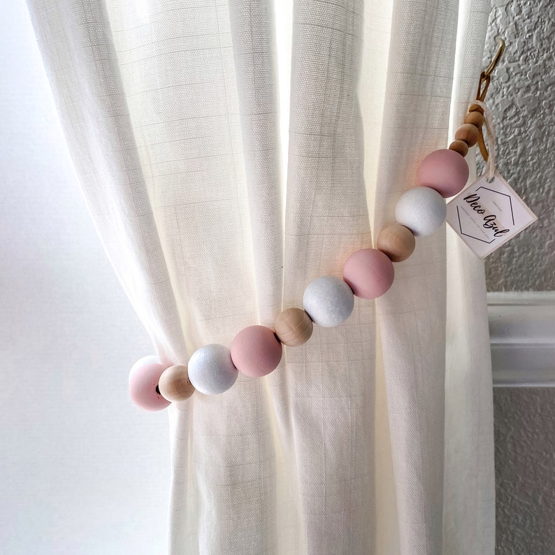 Decorative wooden beads curtain straps tieback with alternating pink, white, and natural wood beads on a textured outdoor curtain.