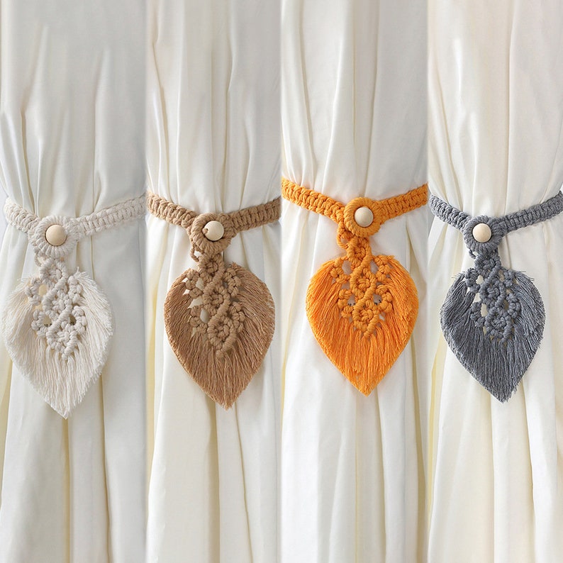 Set of four bohemian macrame leaf curtain tiebacks with wood beads in cream, tan, orange, and grey, on white curtains.
