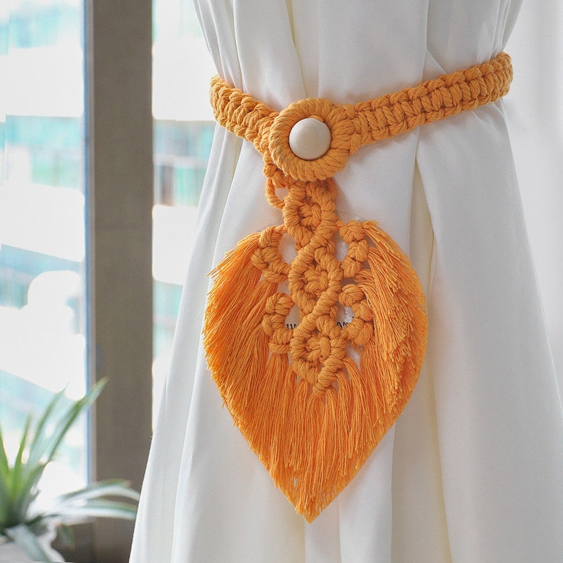 Vibrant orange macrame leaf design curtain tieback with a natural wooden bead securing a white panel