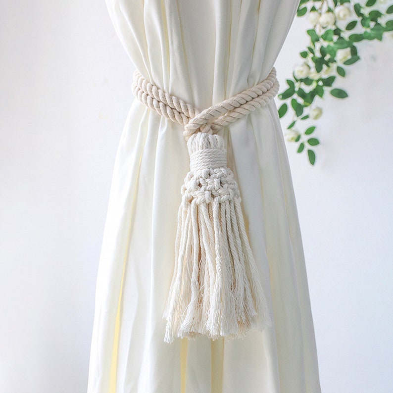 Natural macrame tassel curtain tieback securing a cream patio curtain. Features braided rope & intricate knotwork design.