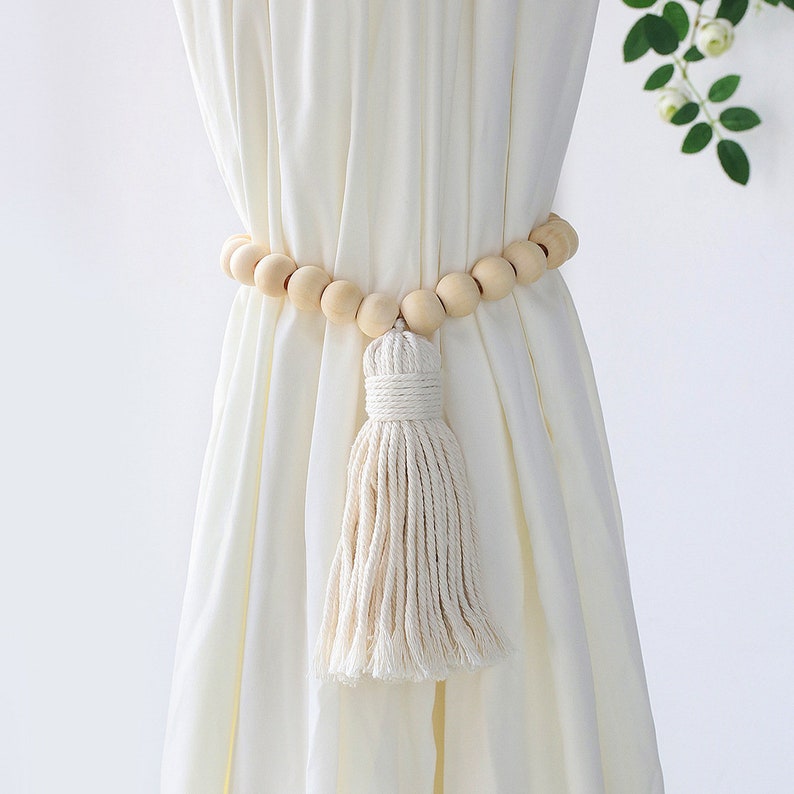 Bohemian macrame tassel curtain tieback with natural wooden beads securing a cream outdoor curtain.