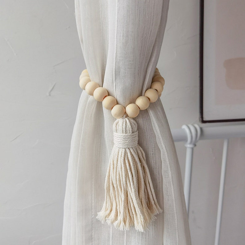 Elegant macrame tassel curtain tieback featuring natural wood beads, styled with a white outdoor curtain for a boho look.