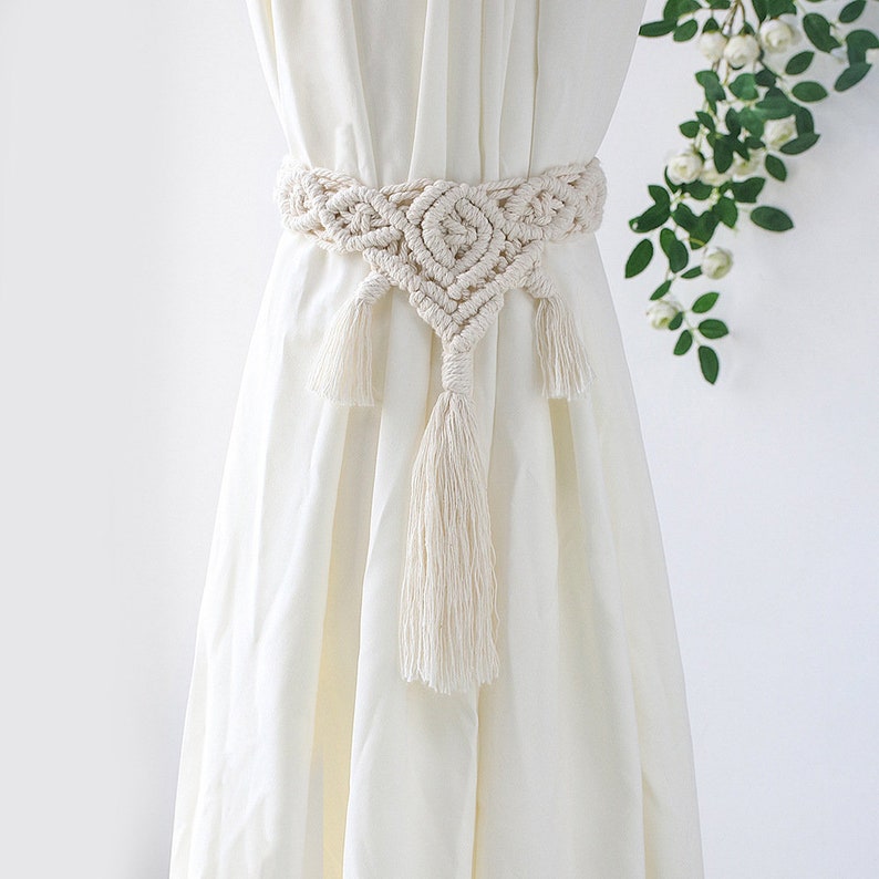 Boho beige macrame curtain tieback with ornate knotting and tassels elegantly holding a white outdoor privacy curtain.