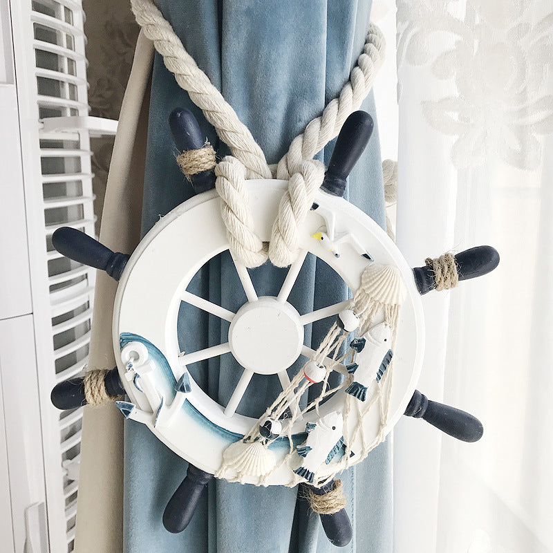 Nautical ship wheel curtain tieback with woven rope, fish, anchor, seashells. Bundles a blue velvet curtain for a coastal look.