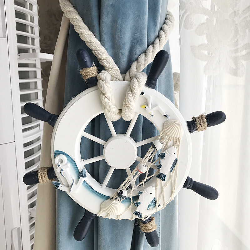 Ship wheel curtain tieback with woven rope strap bundling blue outdoor curtain. Nautical fish, shells, seagulls decor.
