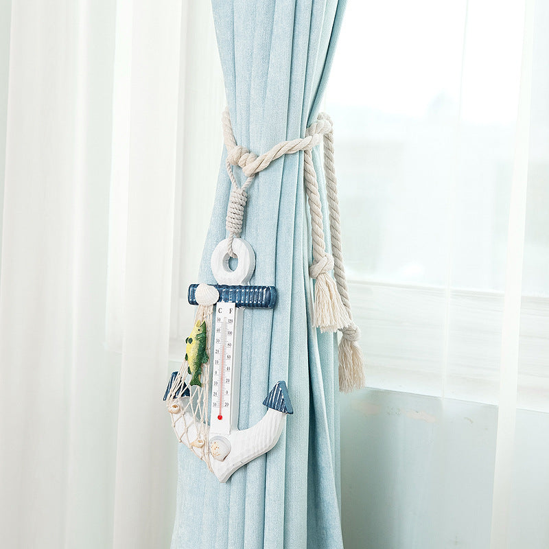 Decorative nautical anchor thermometer on a woven rope curtain tieback, securing a light blue outdoor curtain.