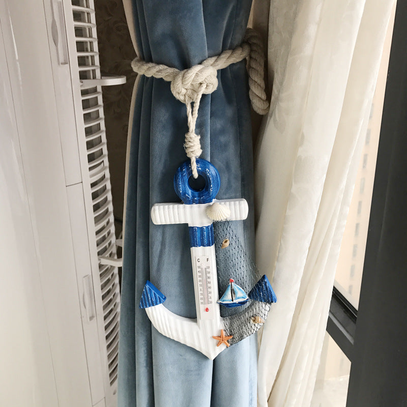 Nautical anchor curtain tieback with a thermometer and sailboat, bundling blue outdoor curtains using a woven rope strap.