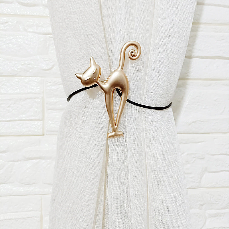 Golden cat magnetic curtain tieback securely holding a sheer white curtain against a white brick wall. Decorative design.