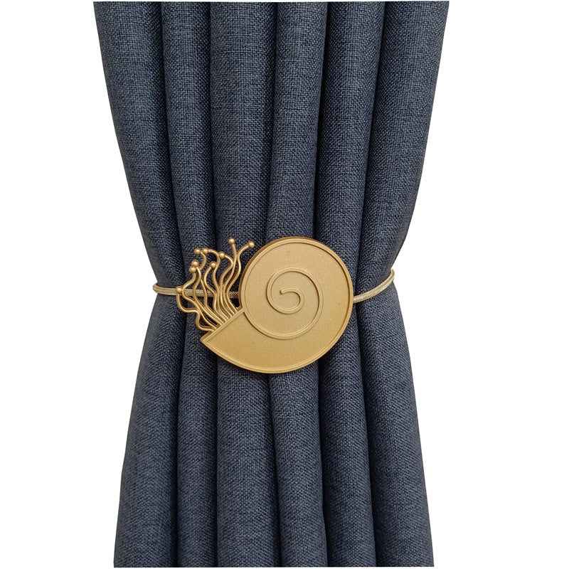 Gold magnetic cat tieback with spiral and whisker-like accents securing a pleated dark blue outdoor curtain.