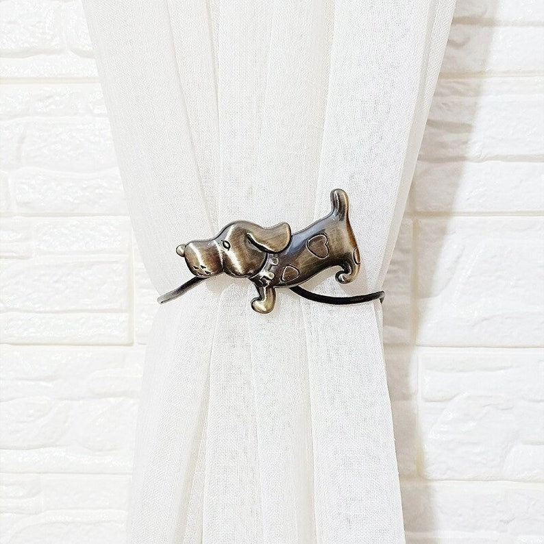 Bronze dog magnetic curtain tieback with heart spots cinching a white sheer curtain against a textured white wall.