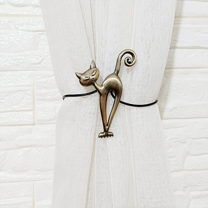 Antique bronze cat magnetic curtain tieback securing a white curtain panel against a white brick wall. Decorative cat design.