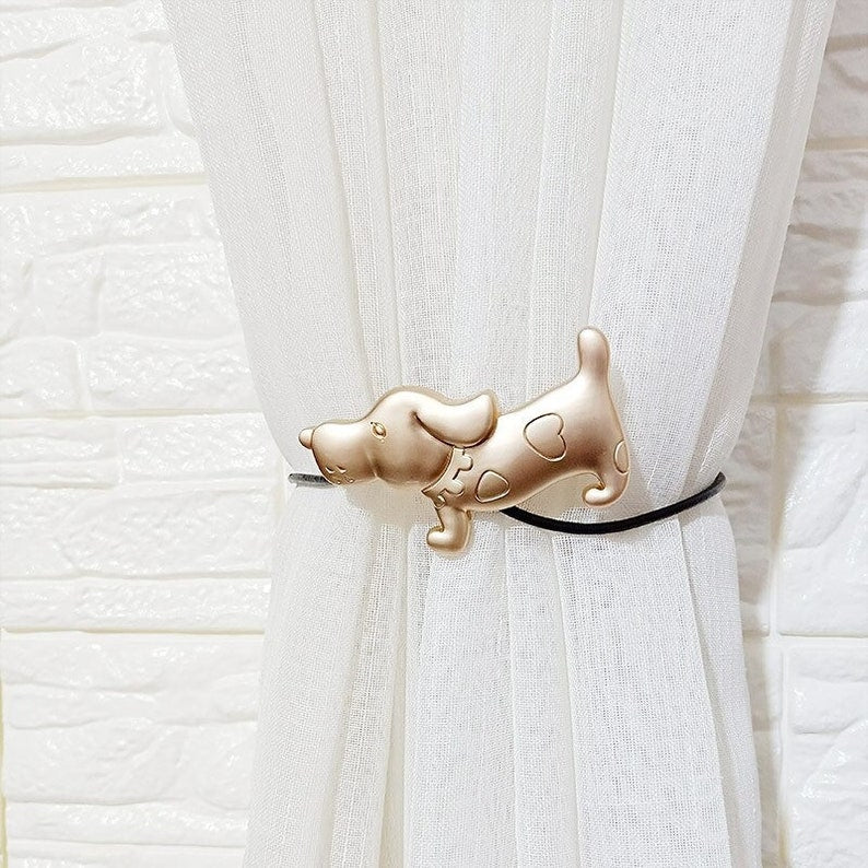 Golden dog magnetic curtain tieback with heart details, stylishly cinching a white sheer curtain against a brick wall.