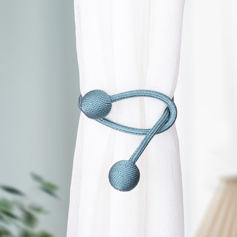 Simple modern teal blue magnetic curtain strap tieback securing a sheer white curtain, braided cord & spherical ends.