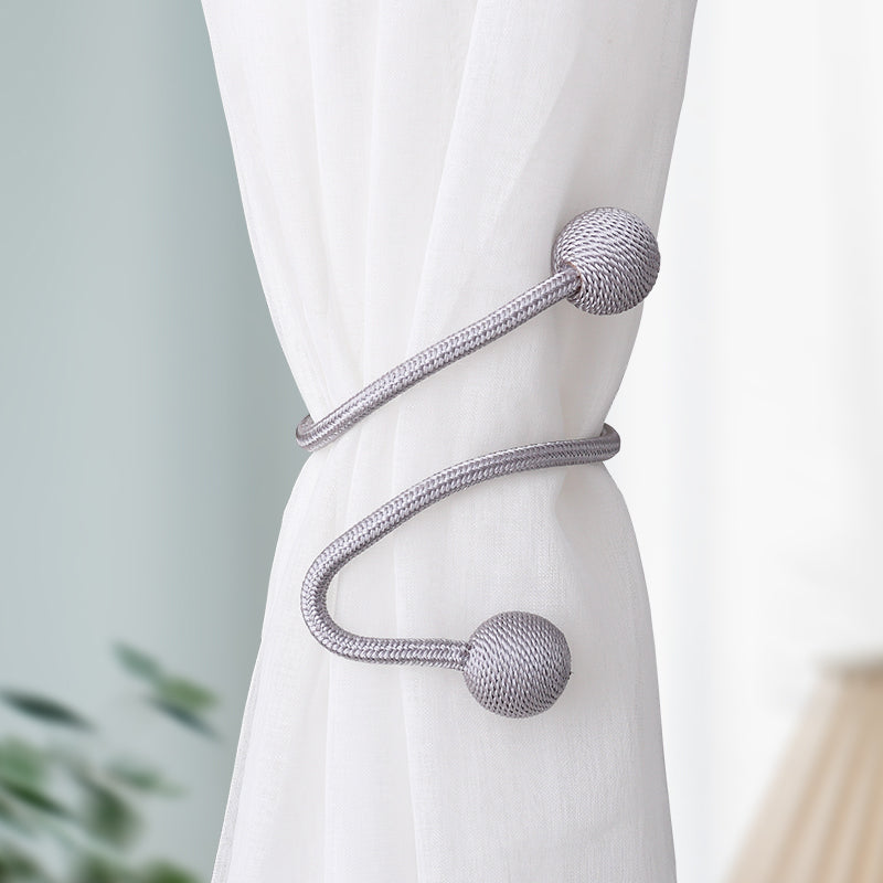 Modern silver magnetic curtain tieback securing a white sheer curtain, featuring braided rope and textured sphere ends.