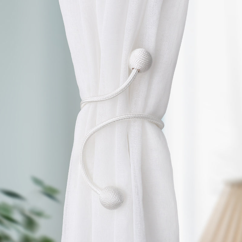 Elegant white flexible curtain tieback with two textured spherical ends, neatly gathering a sheer outdoor privacy curtain.