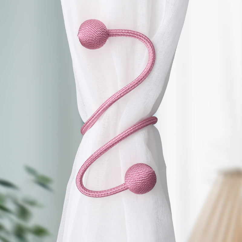 Pink braided magnetic curtain tieback with spherical ends holding a sheer white curtain. Modern, simple design for outdoor spaces.