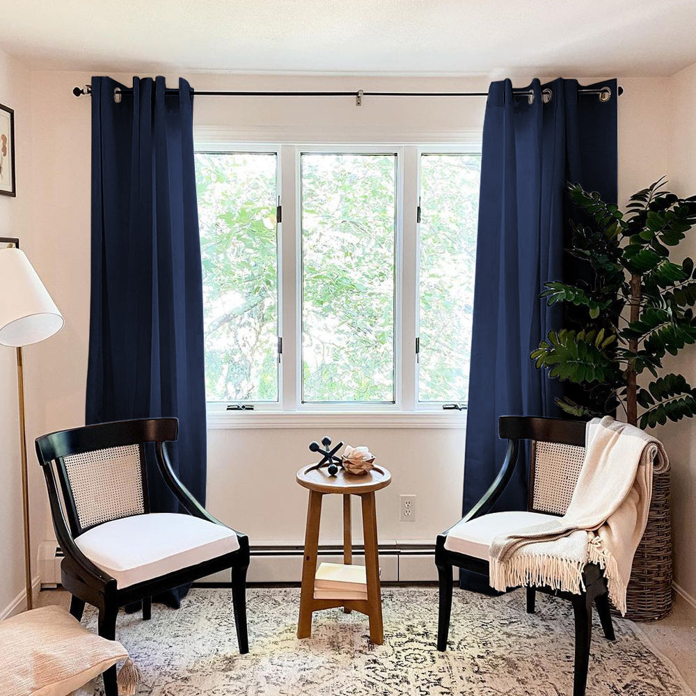 Navy blue grommet thermal insulated blackout weave curtains framing a living room window with two chairs and a side table.