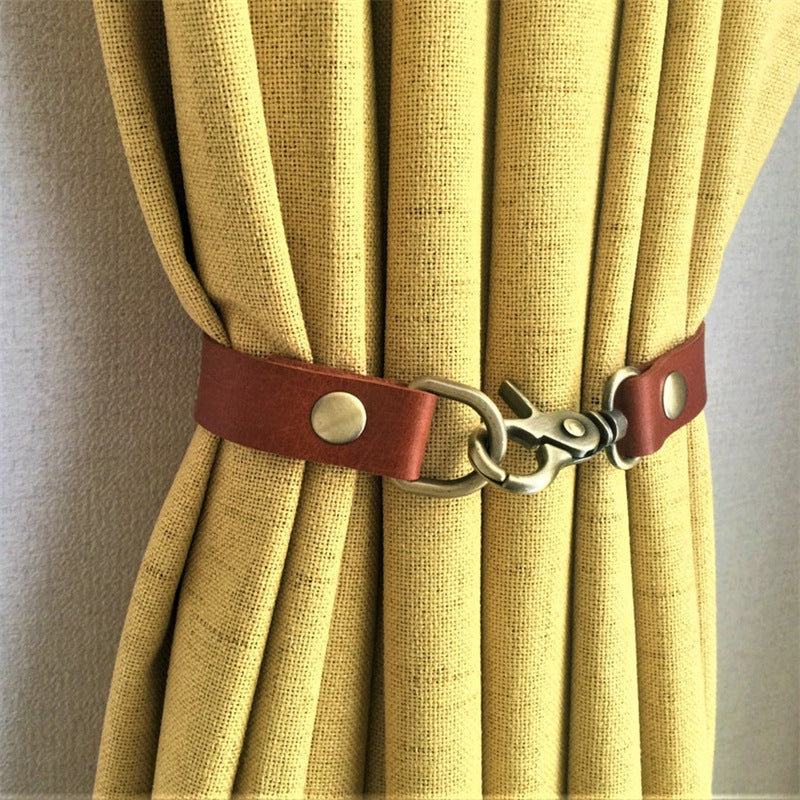 Rustic brown leather curtain strap tieback with metal buckle holding back a pleated yellow outdoor curtain