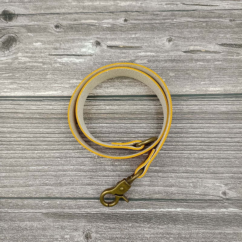 Coiled yellow leather curtain strap tieback with antique brass buckle. Decorative accessory for tying back indoor or outdoor patio curtains.