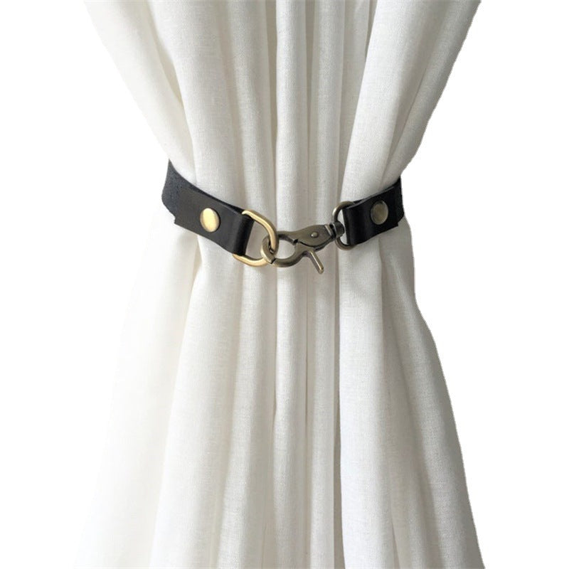 Decorative black leather curtain tieback with brass buckle and hook clasp securing a white curtain, perfect for window decor.