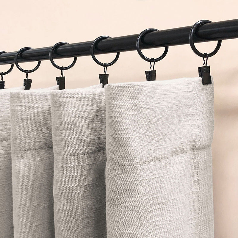 Black curtain rod with black curtain rings and clips holding light grey curtains, perfect for bedroom or living room.