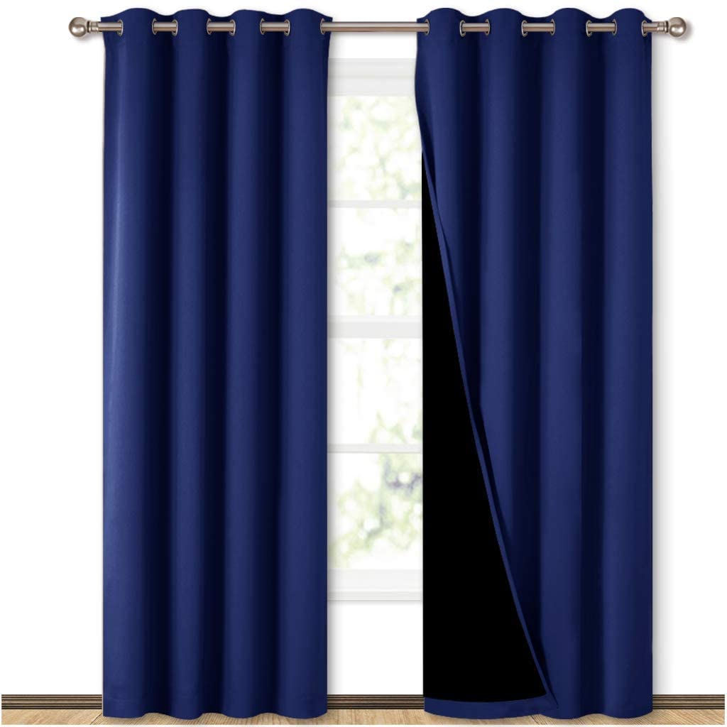 Pair of navy blue double-layer blackout curtains with grommets, one panel exposing its black lining for ultimate light blockage.