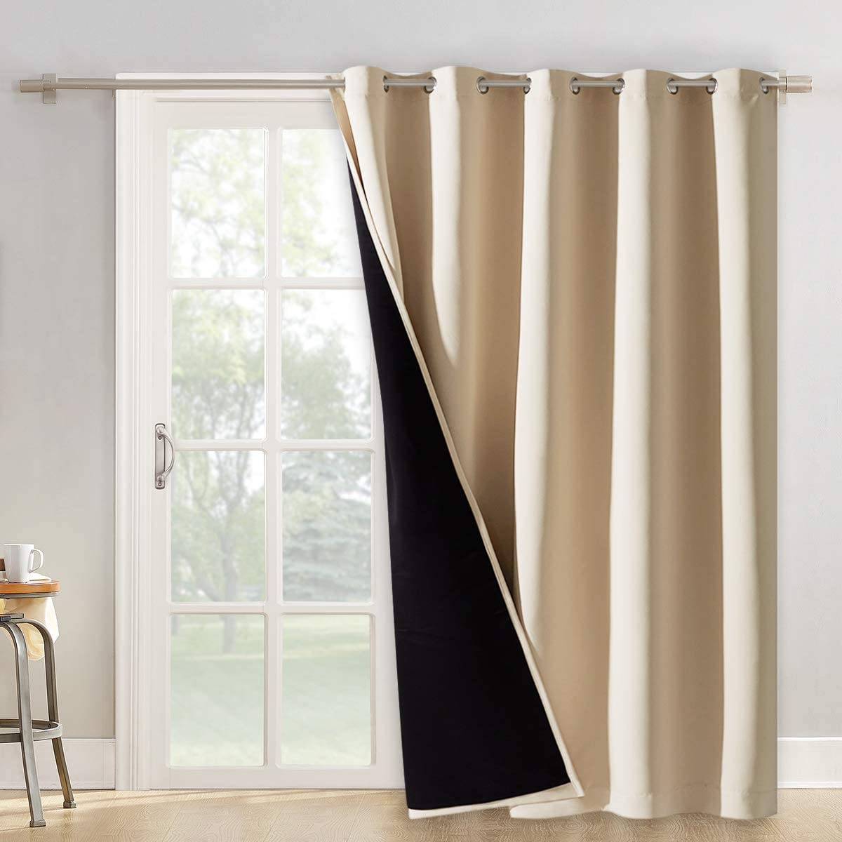 Beige double layer grommet blackout curtain with black lining, partially drawn over a patio door. Ideal noise reducing panel for living room.