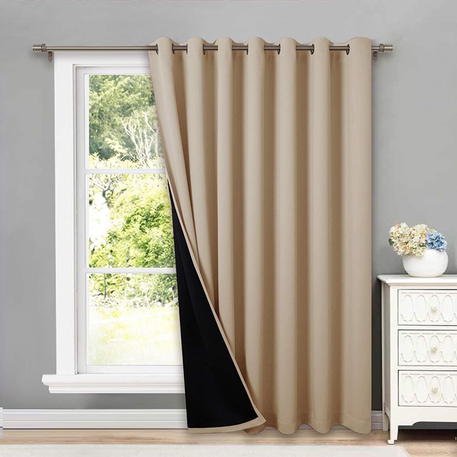 Tan double layer grommet thermal insulated blackout curtain panel, revealing its black lining, hanging in a bright living room window.