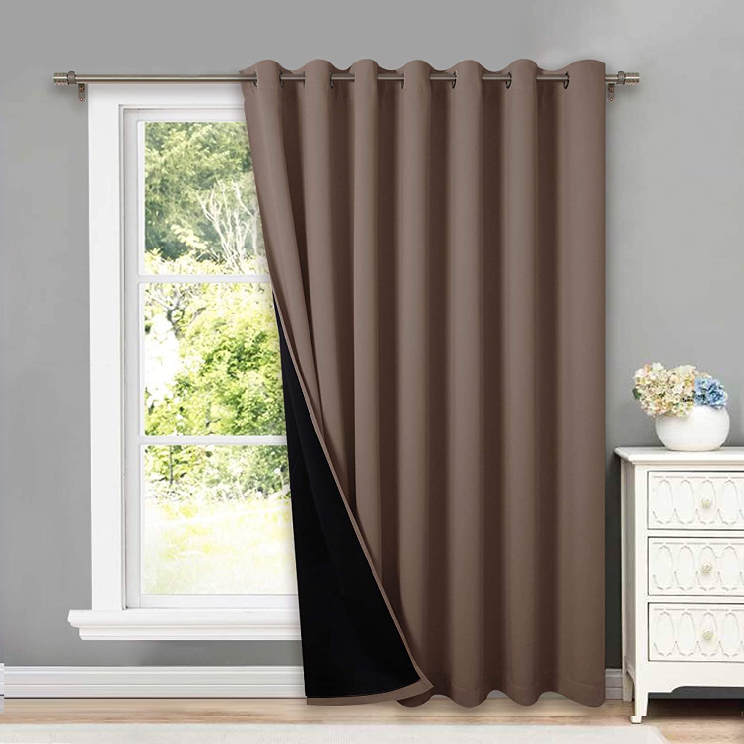 Brown double layer grommet blackout curtain panel, partially open to reveal its black thermal insulated lining, on a living room window.