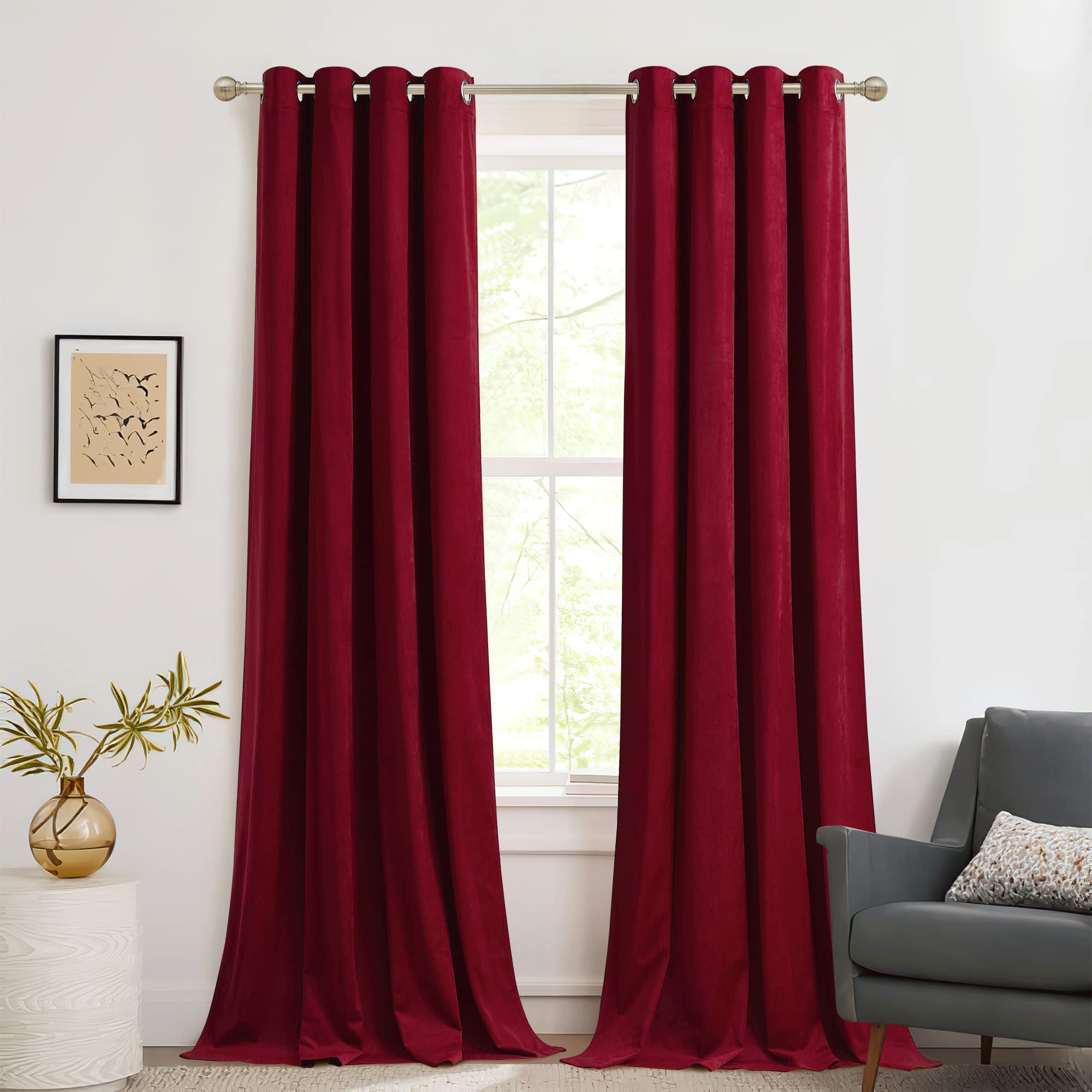 Two rich red velvet blackout curtains with silver grommets hang on a rod, offering room darkening & privacy for a bedroom window.