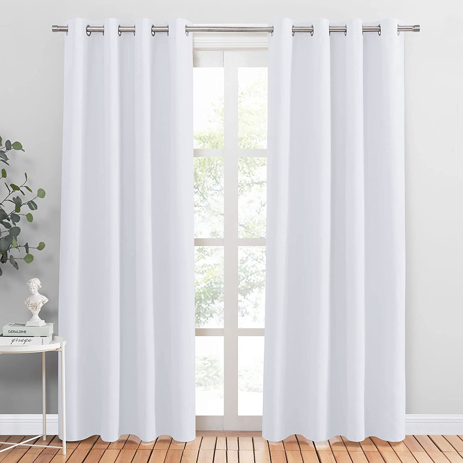 Two white grommet noise reducing blackout curtain panels provide full coverage for a living room or bedroom window.