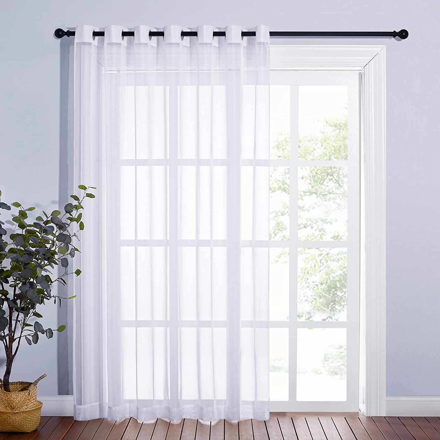 Single white grommet sheer voile curtain panel on a black rod, covering a sliding glass door for bedroom privacy & home decor.