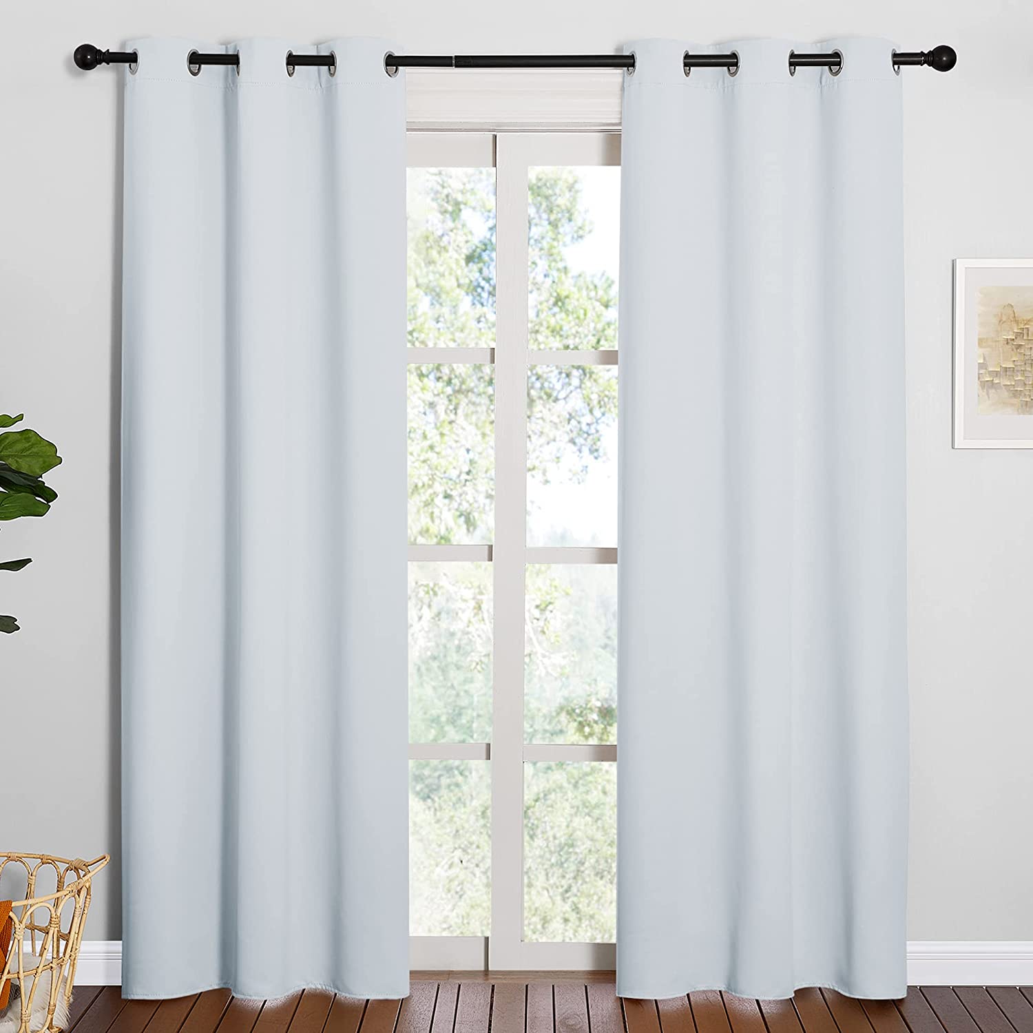 Two light blue grommet thermal insulated blackout curtain panels on a rod in a living room, partially covering a bright window.