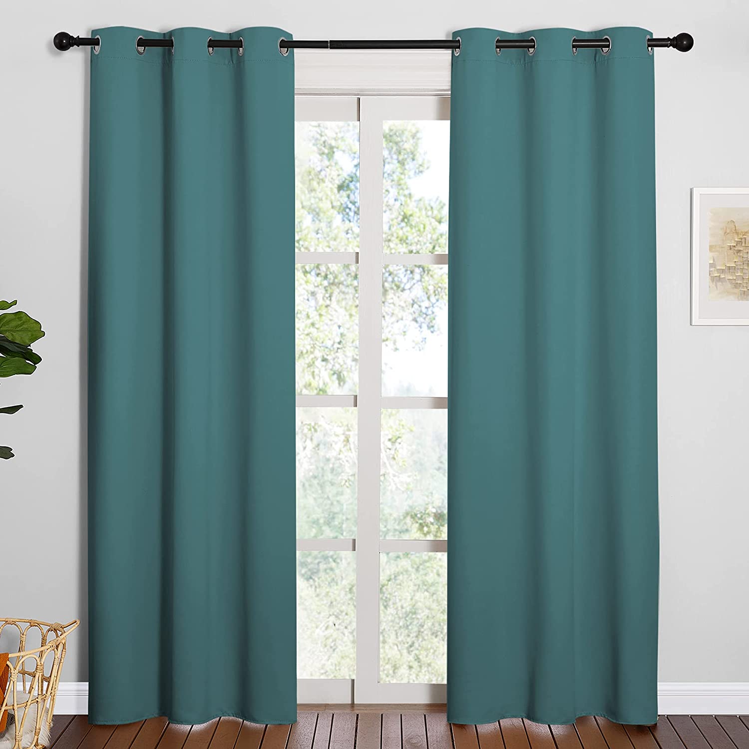 Two teal grommet thermal insulated blackout curtain panels on a rod in a living room, framing an outside window view.