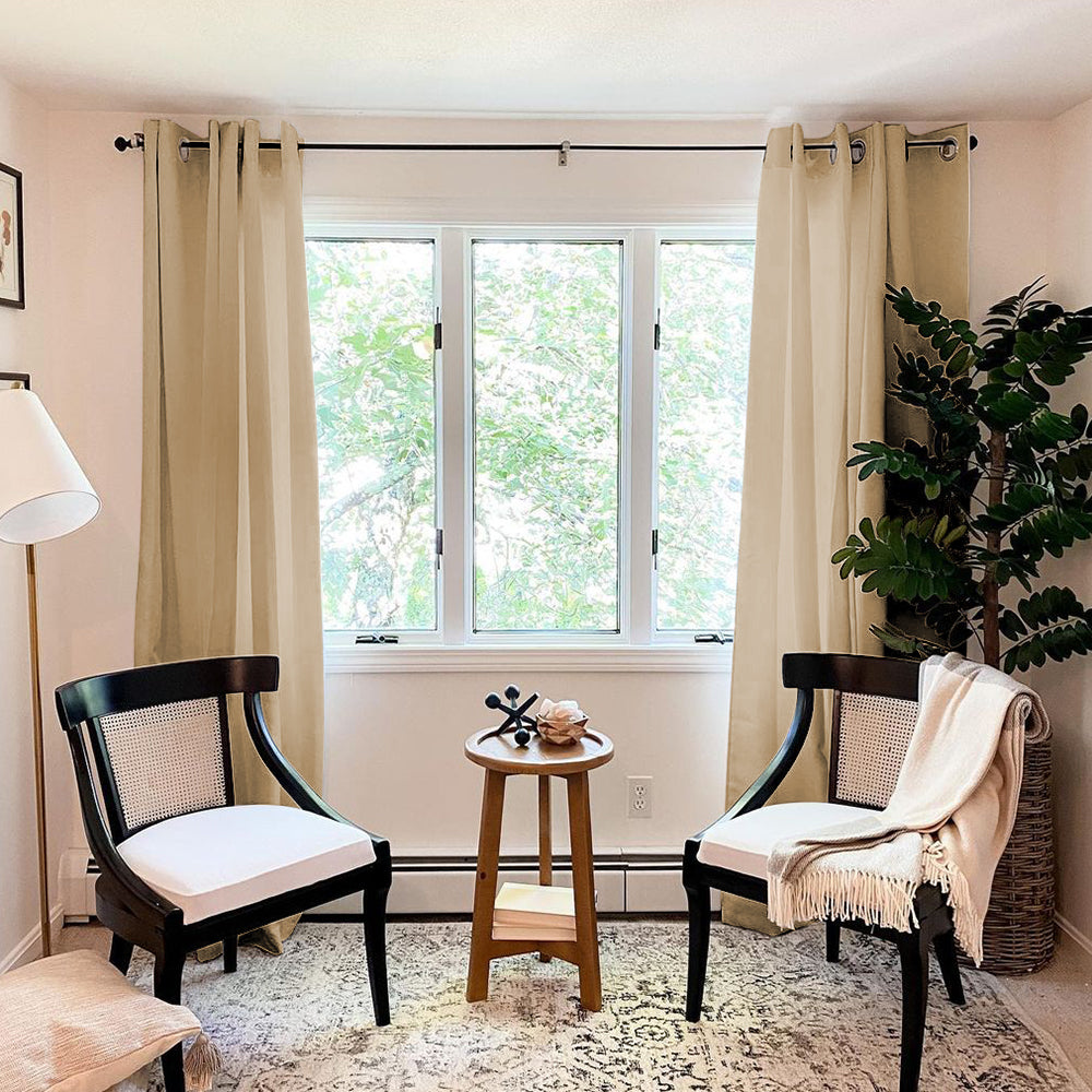 Beige grommet thermal insulated blackout weave curtains, two panels in a living room setting with chairs and a plant.
