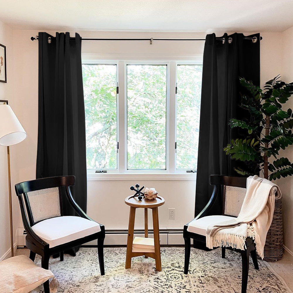 Two black thermal insulated blackout weave curtains with silver grommets hung in a living room window, providing room darkening.