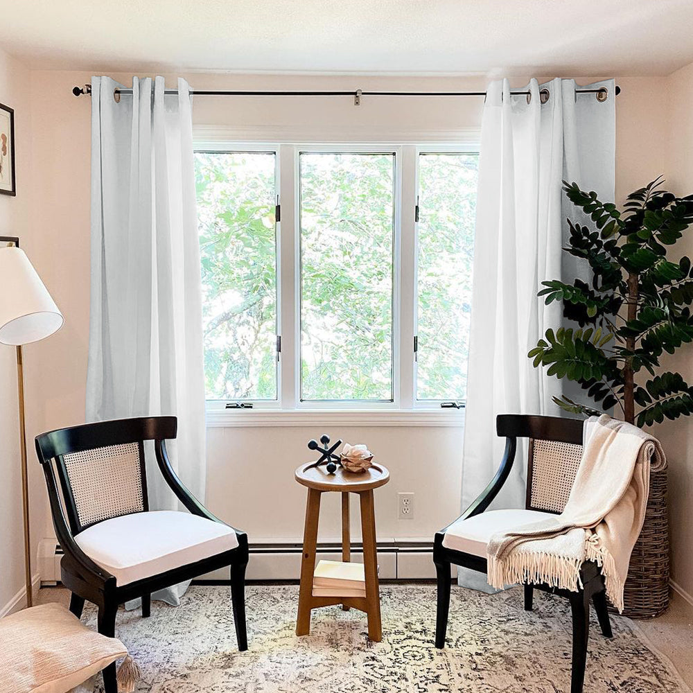White grommet thermal insulated blackout weave curtains covering a living room window, with two chairs and a plant nearby.