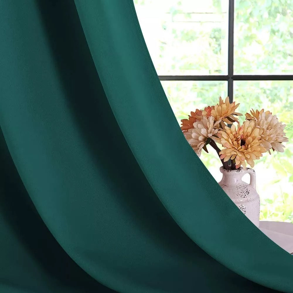 Deep green thermal soundproof blackout curtain panels, softly draped, with a window and vase of flowers in the background.