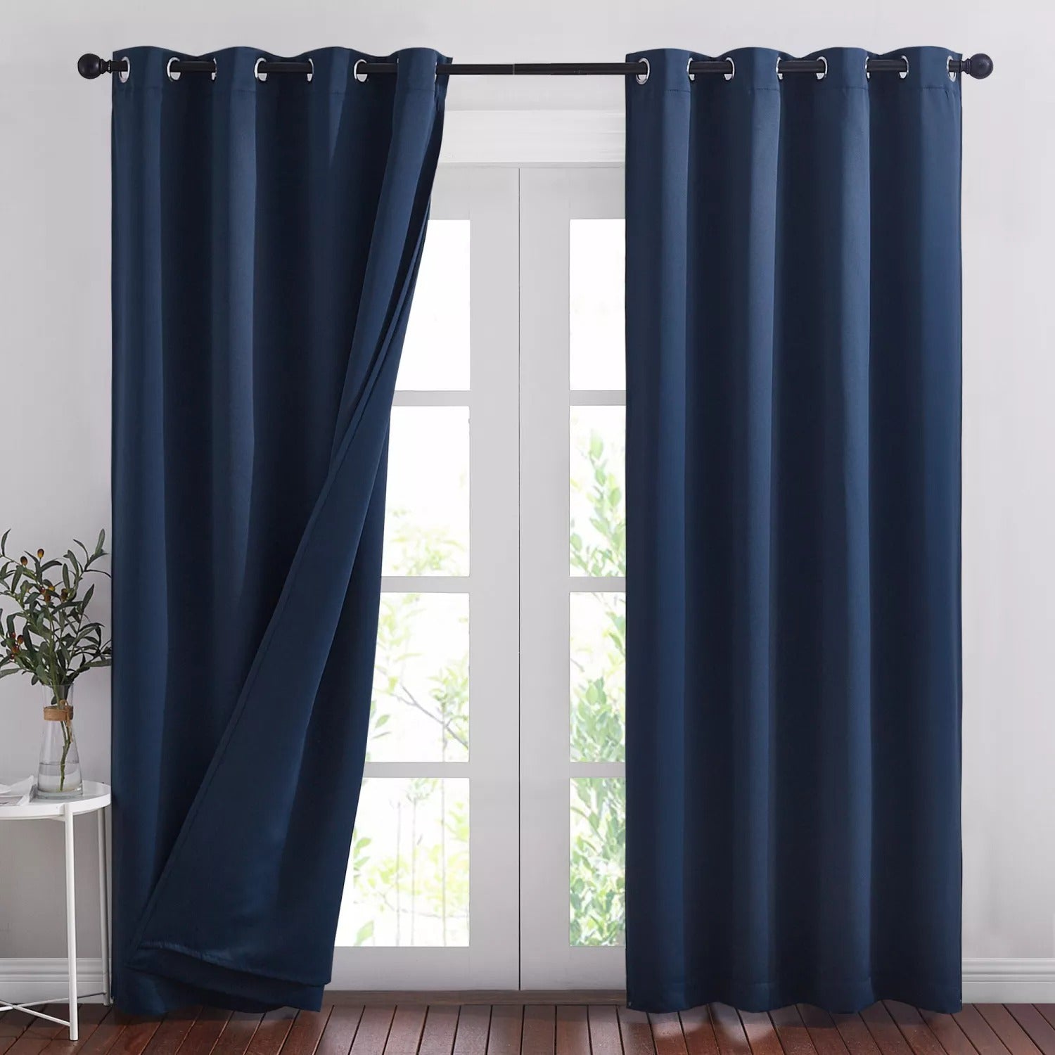 Navy blue 3-layer thermal soundproof blackout grommet curtains in a living room. One panel partially open, one closed, on a window.