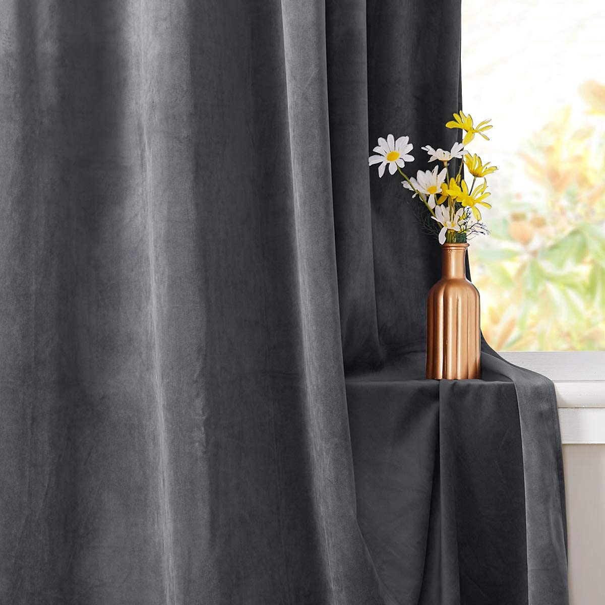 Dark grey velvet blackout privacy curtain panel next to a window with a small vase of flowers on the sill.