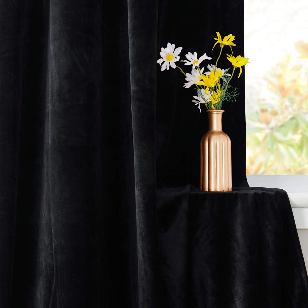 Plush black velvet blackout curtain for bedroom/living room, draped near a window with a vase of white and yellow flowers.
