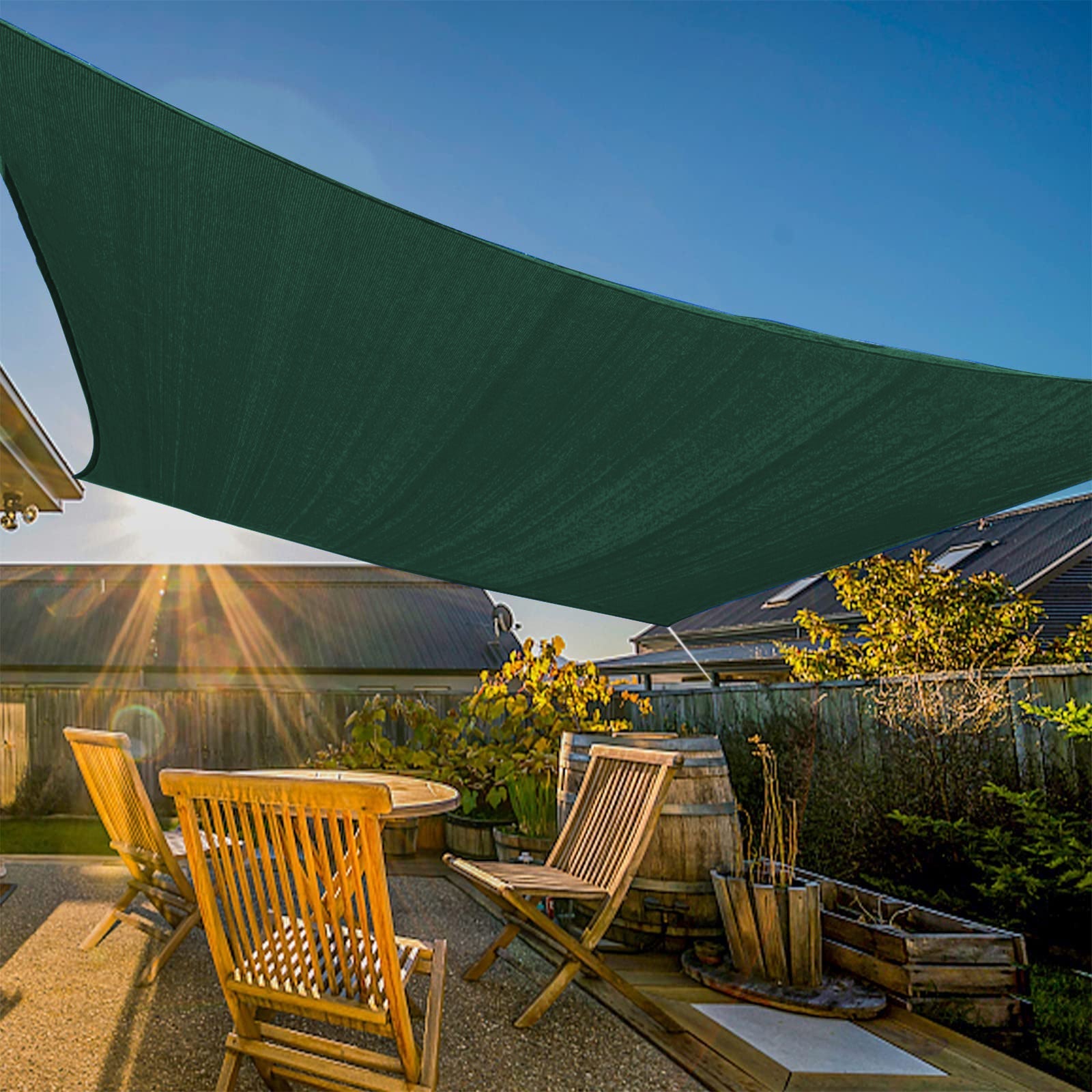 Large dark green triangular sun shade sail providing heavy-duty waterproof sun protection over a patio with wooden furniture and garden at sunset.