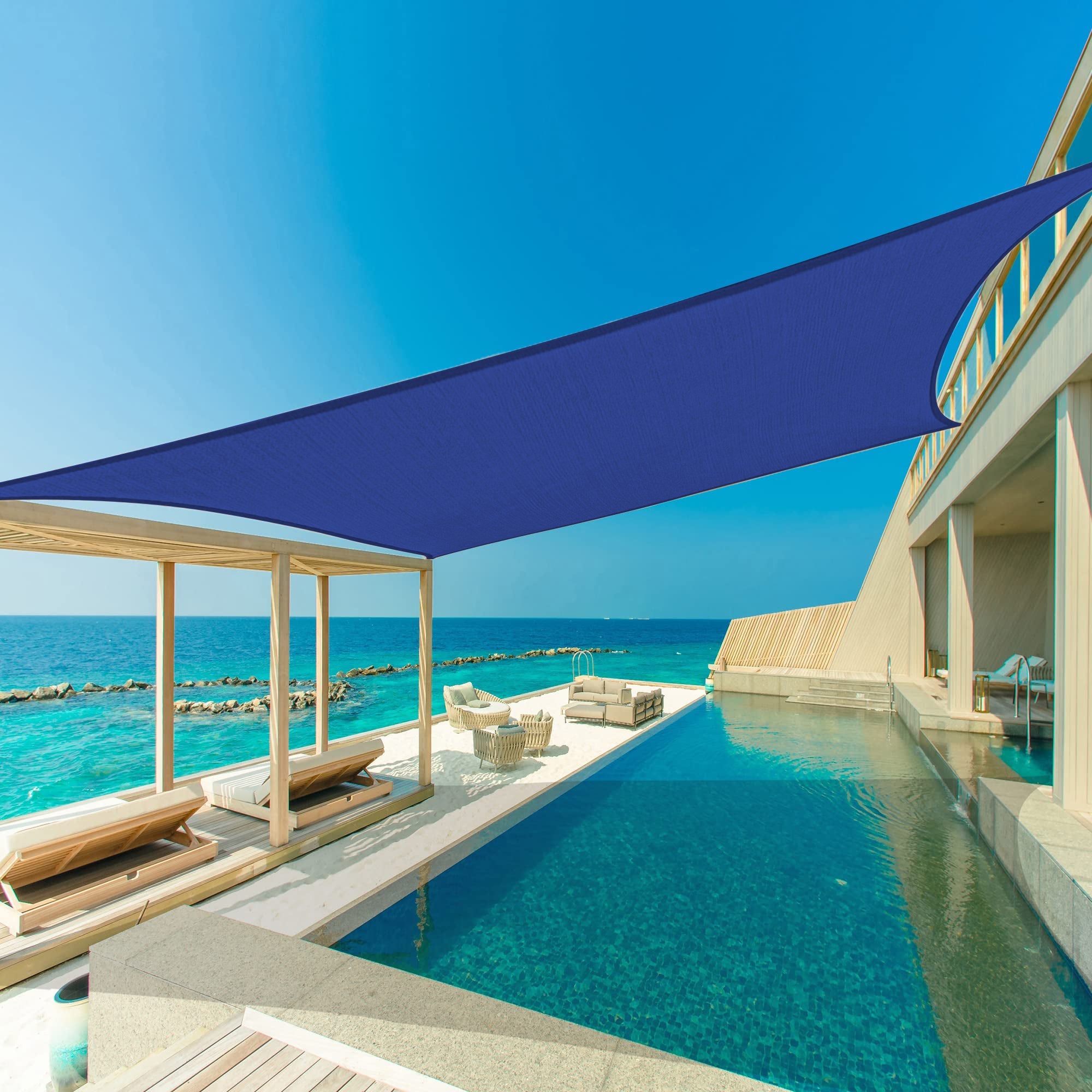 Large navy blue heavy duty sun shade sail providing a waterproof awning canopy over a luxurious patio with infinity pool and ocean.