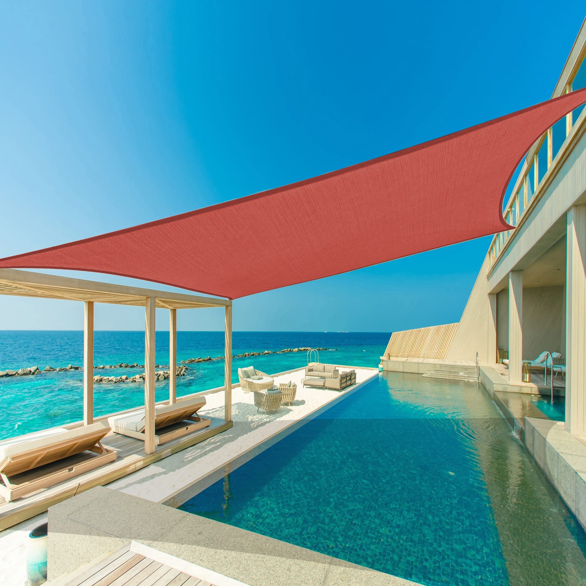 Red heavy-duty sun shade sail provides waterproof shade for a luxurious patio with infinity pool & ocean view. Perfect for outdoor living.