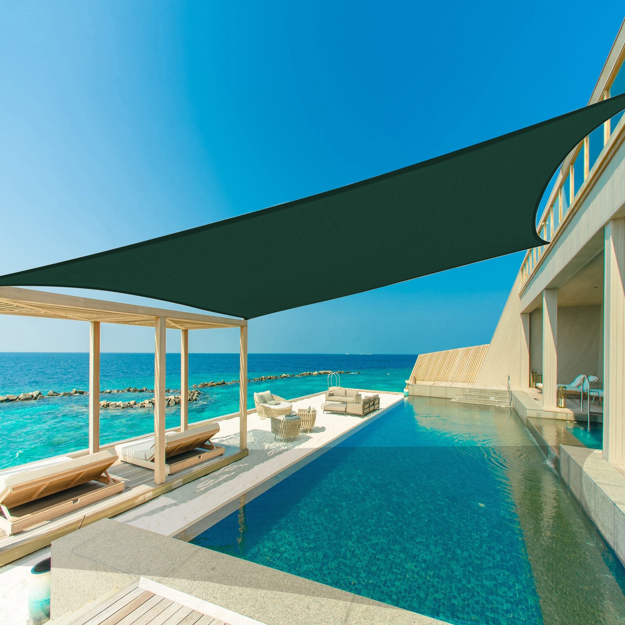Large, heavy-duty dark green sun shade sail providing waterproof protection over an elegant patio, infinity pool, and ocean.