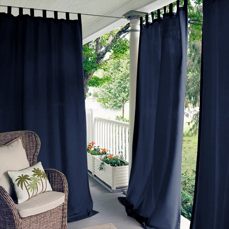 Navy blue tab top waterproof outdoor curtains on a porch deck, providing shade and privacy for a wicker chair.