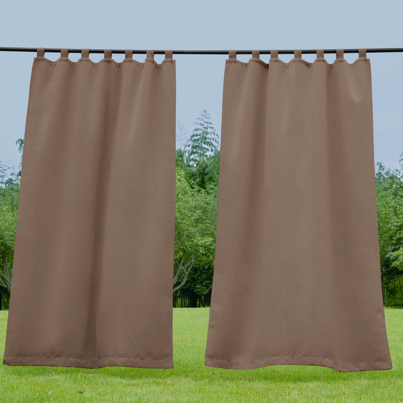 Two brown waterproof tab top outdoor curtains hanging on a rod, with a green grassy lawn and trees in the background.