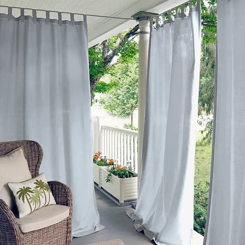 Porch deck with light grey waterproof tab top outdoor curtains providing privacy, next to a wicker chair.